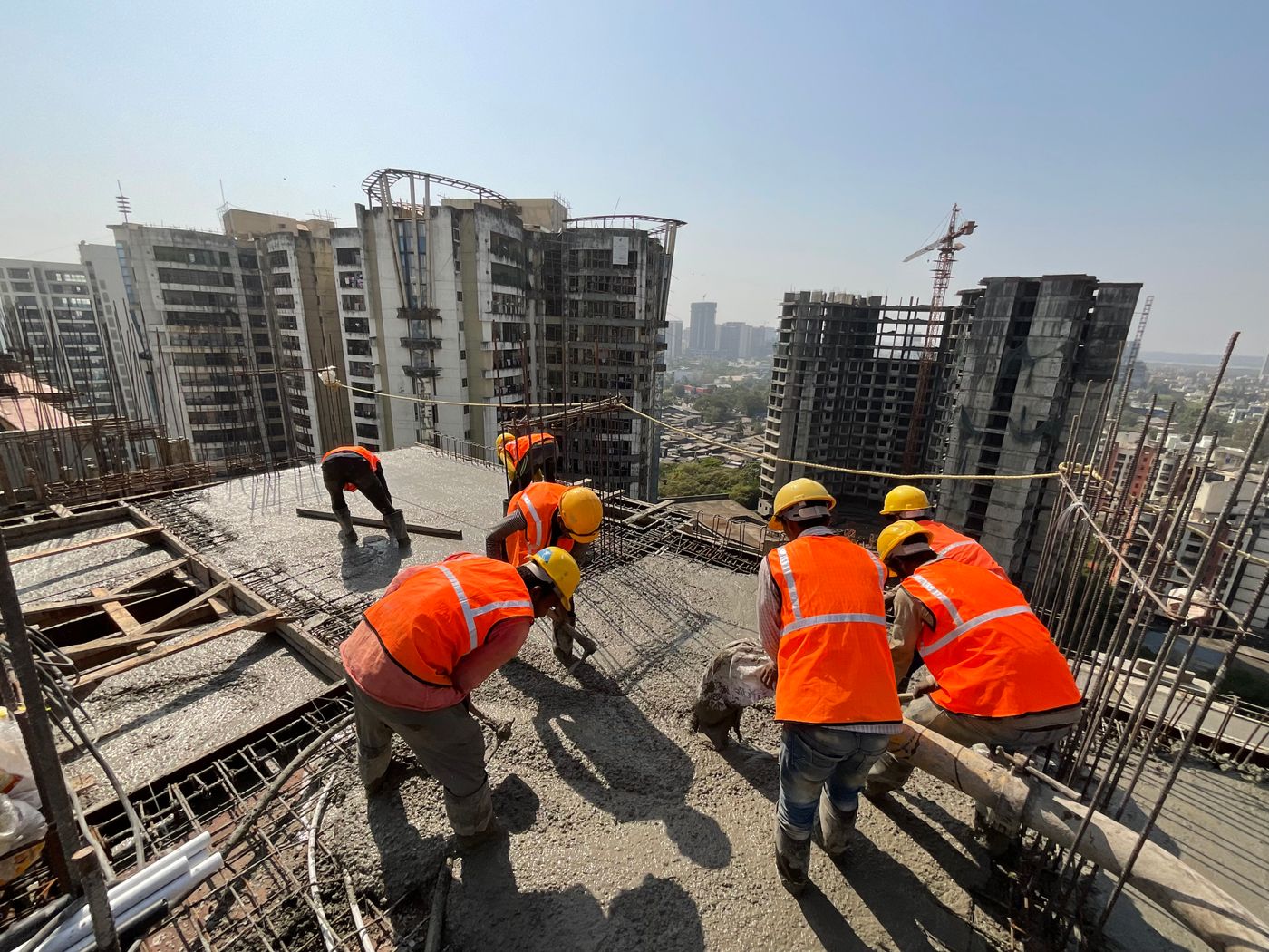 Construction workers in safety gear on a high-rise slab, with towers behind